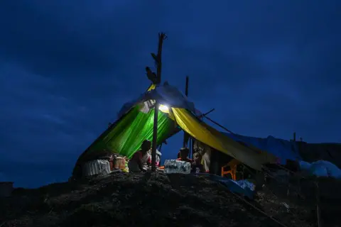 Getty Images Flood affected residents shelter inside a temporary tent after being displaced by flooding on August 4, 2026 in Sivasagar district, Assam, India.