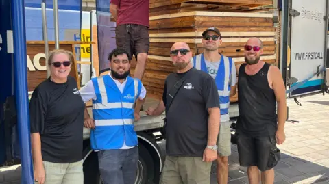 Aisha Iqbal/BBC A woman and four men stand beside a flatbed truck smiling
