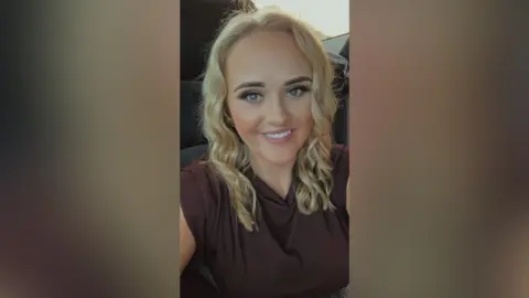 Maelisa McGettigan Maelisa is taking a selfie. She has blond hair that is styled in curls. She's wearing a brown top. 