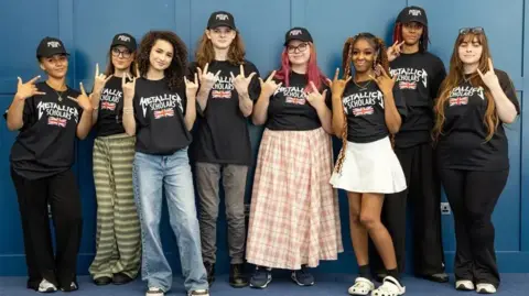 Capital City College A group of students look to camera and make rock hands whilst wearing t shirts saying Metallica Scholars 