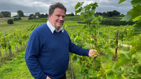 Martin Fowke from Three Choirs Vineyard stood holding some grapes on the vine on a cloudy day