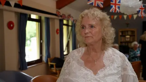 Former resident Halina Grabiec. She is wearing a white blouse and has long blonde curly hair. 
