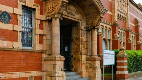 Westmorland and Furness Council The entrance to Nan Tait Centre - a red brick building with columns either side of the stepped entrance. There are leaded windows flanked by sand coloured stonework.