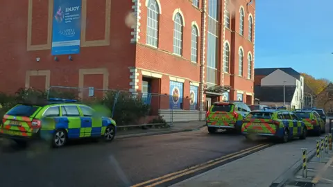 Contributed A number of police vehicles line a street outside of a former casino building in Commercial Street in Northampton. It is a sunny day. There is a blue sky.