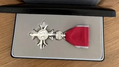Mike Davies A silver MBE medal with a red ribbon in a black presentation box