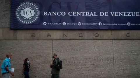 People in Caracas walk past the facade of the central bank. A banner on the front of the building reads Banco Central de Venezuela.