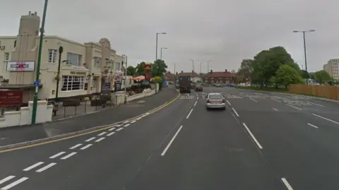 A four-lane road with a whitewashed pub and hotel building next to it