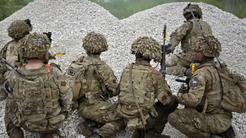 Soldiers in camouflage crouching by gravel 