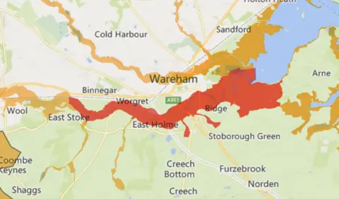 Environment Agency Environment Agency map of the Wareham area showing flood alert areas in orange and flood warning areas in red. A large area surrounding the river that runs from Poole Harbour, south of the town, is marked in red.