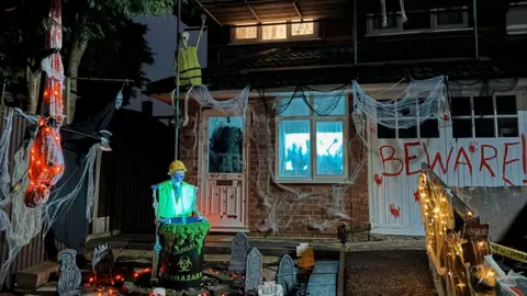 Jodie Fisher skeletons wearing high-vis jackets, BEWARE, painted with fake blood on garage doors, tombstones and cobwebs on the front of the house. 