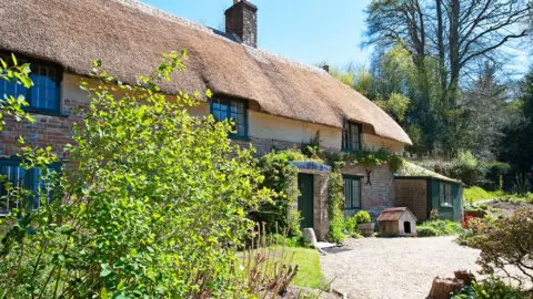 Thomas Hardy's cottage three-quarter view, Thorncombe Wood, Dorset, England. Bright tranquil Spring days highlight the blue skies and rich colours of the English countryside and contrast with the traditional old style of building architecture found in the cottages, homes and landmarks of the idyllic Dorset landscape, such as the author Thomas hardy's cottage here, location for books such as Far From the Madding Crowd.