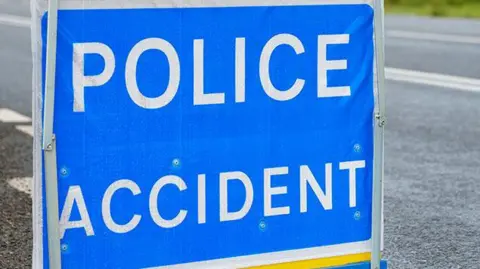 Police accident sign, white writing on blue sign, with a road in the background