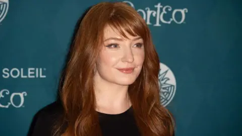 Getty Images Nicola Roberts, a woman with long ginger hair and a fringe. She is smiling, and looking to the right of the image. She is wearing a black top.