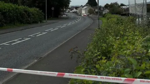 BBC It shows a police tape and an empty road on the edge of a village 