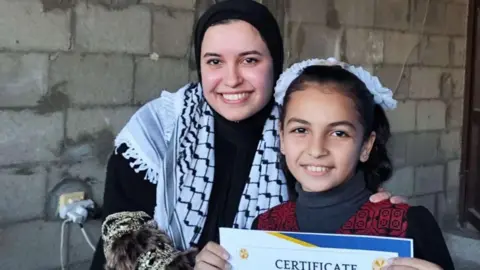 Sana el-Azab Sana el-Azab with a student, who is holding up a certificate of achievement, in central Gaza
