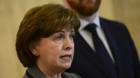 Pacemaker Diane Dodds has short reddish brown hair and is speaking at a oress conference in the picture 