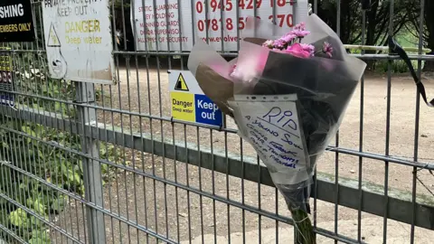 Tom Jackson/BBC The floral tribute from local residents on a fence. A piece of paper attached the flowers reads: "RIP, a young soul, gone forever, our thoughts and prayers."