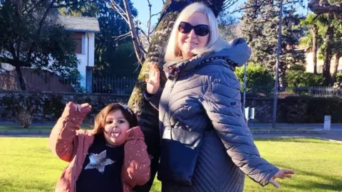 Chiara Del Vescovo Chiara Del Vescovo and her daughter hold their arms out as they pose next to a tree in a park