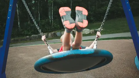 A child on a basket swing with their feet in the air.