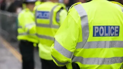 Police officers facing away from the camera with hi vis jackets on with Police written on the back