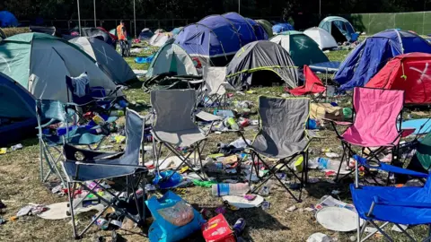 Jess O'Riley A festival site showing lots of abandoned tents, camp chairs and rubbish strewn across the grass