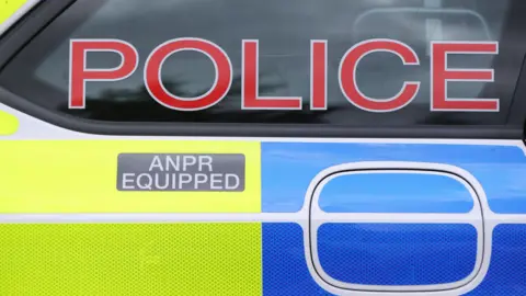 PA Media A close-up shot of the side of a police car. There are reflective yellow and blue stickers on the car, a grey sticker which says ANPR equipped and a red 'Police' sign on the window