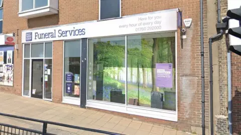 Google Co-op Funeral Services building in Swaffham. It is a yellow brick building with large glass windows and a glass door entrance. The name of the funeral parlour sits above the entrance. 