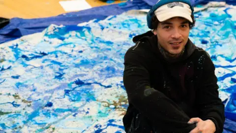 Leicester BID Artist Marcus Dove sat beside a large abstract blue painting spread out on a floor.