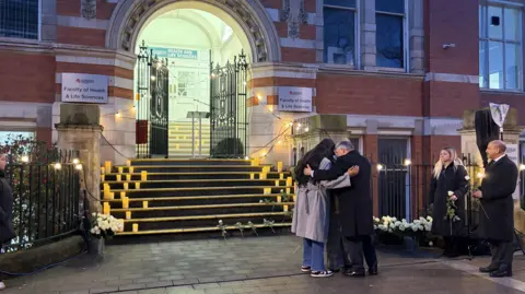 A group of people hug at a vigil on the De Montfort University campus