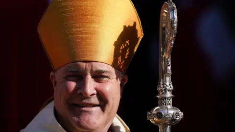 Getty Images The Archbishop of York, smiling on a sunny day. He is wearing a bishop's mitre and is holding a crosier.