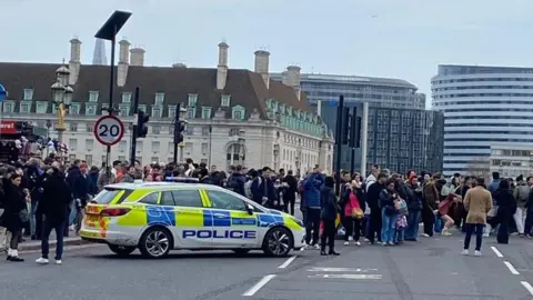 A police car has stopped on Westminster Bridge and people are stood all around it in the background