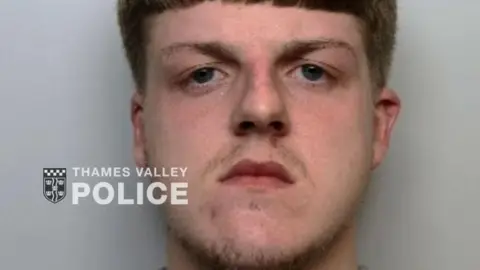 Thames Valley Police A police custody photo shows Lewis Collier with straight, red-brown hair and a wispy moustache and goatee beard.