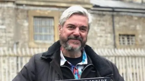 Dave Cable Dave Cable has grey hair and a salt and pepper beard and is standing outside Shepton Mallet prison