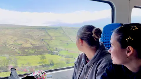Nick Wooley/BBC Two young women look out of the window to see green rolling hills