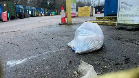 Clare Cowan / BBC  A recycling centre with a white bag of rubbish on the floor.