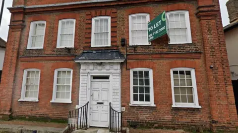 A large two storey building with a white door and several windows with a To Let sign outside.