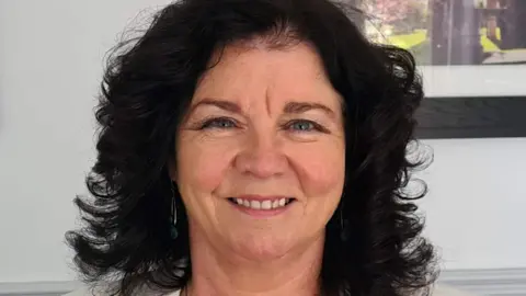 Donna Fox Donna Fox, a woman with shoulder-length curly black hair, smiling at the camera. She has blue eyes and is wearing earrings and a white suit jacket. 