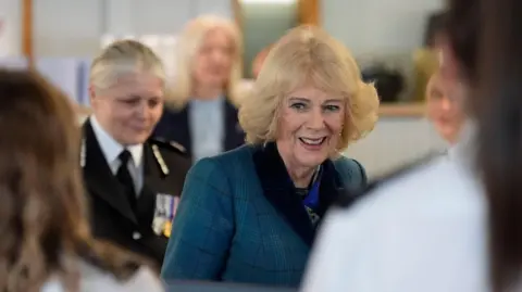Queen Camilla walks through an office at the Avon and Somerset Police headquarters, where she is greeted by some of the staff.