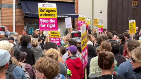 BBC A crowd gathered outside Asylum Welcome in Oxford, holding banners reading: "Refugees are welcome. Stop the extreme right".