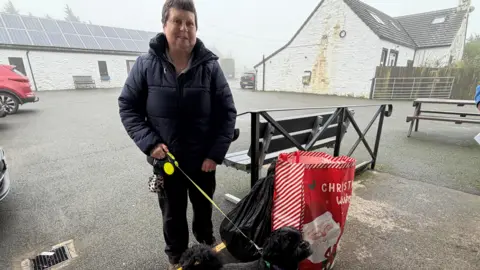 A woman in a navy jacket with a small black dog on a lead.