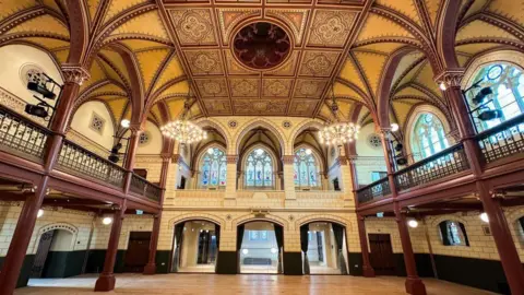 Dover District Council A regal main hall of a building. There is a unique pattern on the roof along with two chandeliers.