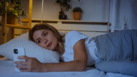 Getty Images Woman lies in bed at night looking at her smartphone