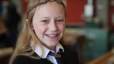 Olivia smiling at the camera in a school classroom