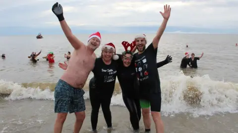 St Elizabeth Hospice Two men and two woman standing in the sea while laughing and smiling