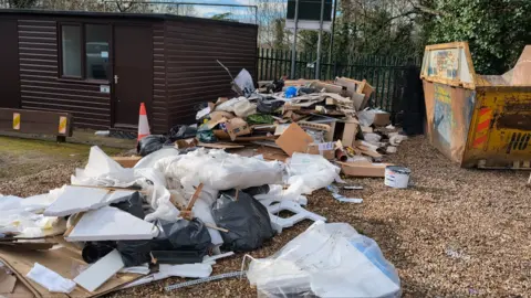 A huge pile of rubbish, including black bags and bits of wood, discarded on the ground.