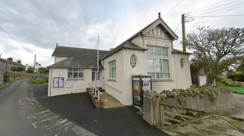 Sockbridge and Tirril Town Hall. The building is white with a slate roof. A sign above the main windows says, Reading Room and Library 1914.
