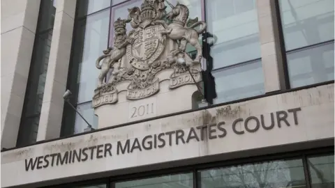 The words 'Westminster Magistrates Court' are mounted on pale stone above the court entrance. Above that is a sculpted coat of arms.