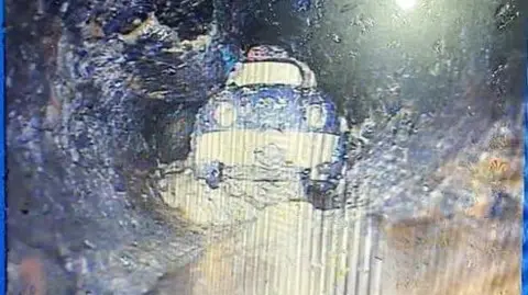 South West Water The toy car pictured in a drain. It appears to be a blue and white plastic car and is sitting in sludge.
