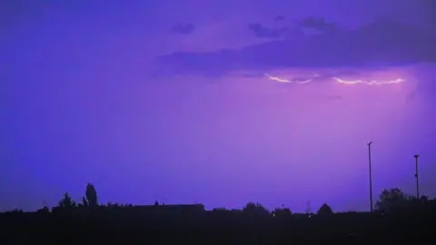 Mark Griffiths Lightning forks seen in purple sky over buildings in the shadow 