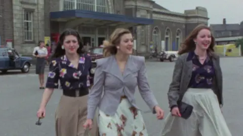 Three young women in 1970s fashion, walking out of Margate train station.
